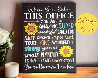 May include: Black canvas sign with white text that reads "When You Enter This Office You Are Amazing Super Wonderful Cared For Safe Brave Important Tough Kind Wonderful Strong Special Smart Respected Extraordinary Understood You Are The Reason I Am Here". The sign has two yellow sunflowers with brown centers. The text "Customize Canvas" is in a yellow circle in the upper right corner.