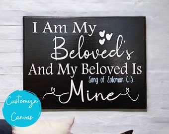 May include: Black canvas wall art with white text that reads "I Am My Beloved's And My Beloved Is Mine" with a small heart design on either side of the text. The text "Song of Solomon 6:3" is written in smaller white text below the main text.