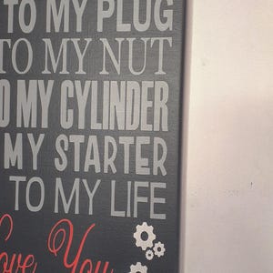 A close-up, angled view of the black canvas sign with red and gray text, showing the bottom right portion of the text and gear graphics.