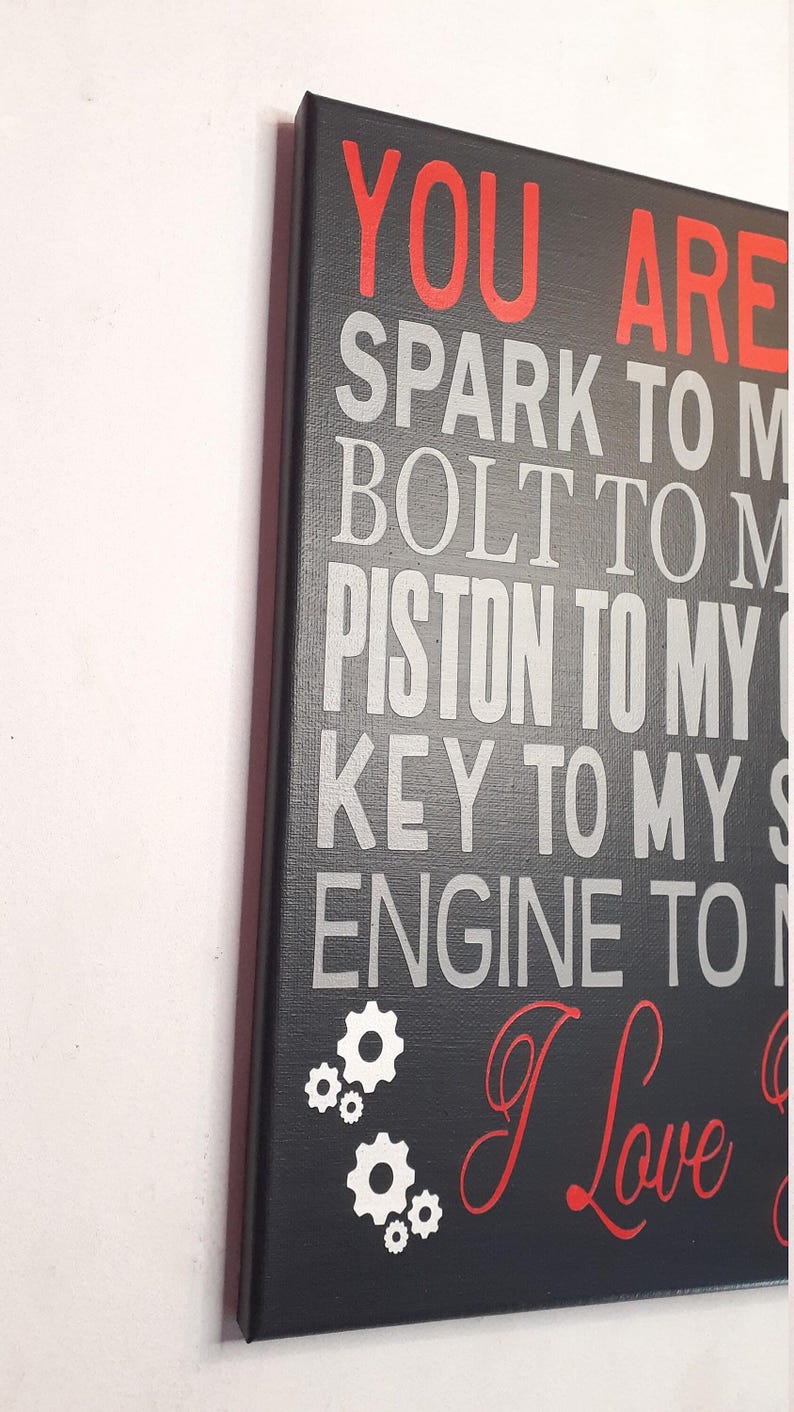 A close-up, angled view of the black canvas sign with red and gray text, showing the side edge of the canvas.