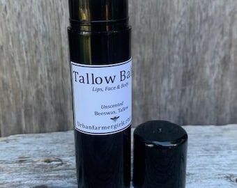 May include: A black lip balm tube with the cap off, revealing the product. The label reads "Tallow Balm" and lists ingredients. The balm is unscented and for lips, face, and body.