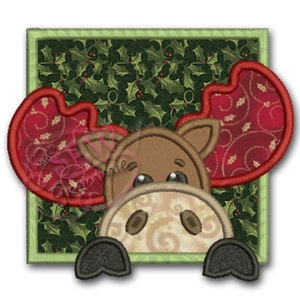 May include: A brown moose with red antlers peeking out of a green holly-patterned square frame. The moose has large brown eyes and a brown nose.