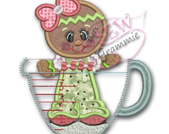 May include: A gingerbread person wearing a green and white dress and a pink bow is standing inside a green measuring cup. The cup has red markings on the side.