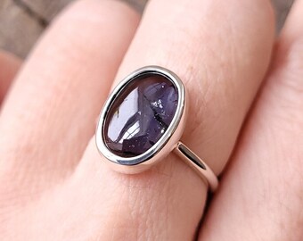 May include: A silver ring with a dark purple oval gemstone set in a bezel setting.