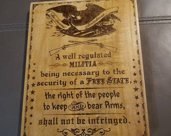 May include: A wooden sign with a brown background and black text. The sign features an eagle with outstretched wings and the text "The Second Amendment". The text below reads "A well regulated Militia being necessary to the security of a FREE STATE, the right of the people to keep AND bear Arms, shall not be infringed."