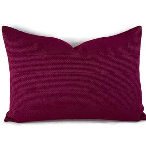 May include: A rectangular decorative pillow in a deep magenta hue. The pillow has a textured woven fabric and is set against a white background. This accent pillow is designed for home decor.