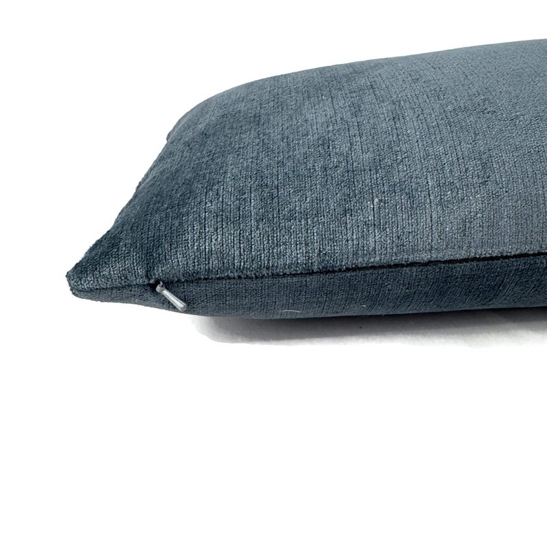 Puede incluir: Una funda de coj&iacute;n rectangular en un color azul pizarra profundo con un acabado de tela texturizada similar al terciopelo. El coj&iacute;n cuenta con una cremallera azul a juego visible a lo largo de la costura lateral, aportando un dise&ntilde;o limpio.