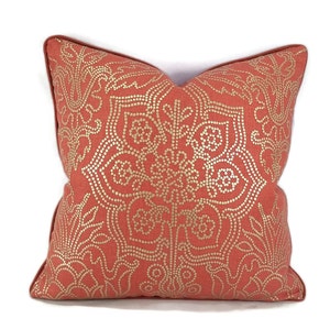 May include: A coral colored throw pillow with a gold mandala design. The pillow is made of a soft, textured fabric.