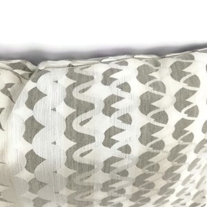 Puede incluir: Una almohada blanca con un patr&oacute;n geom&eacute;trico gris. El patr&oacute;n est&aacute; formado por formas curvas que se repiten.