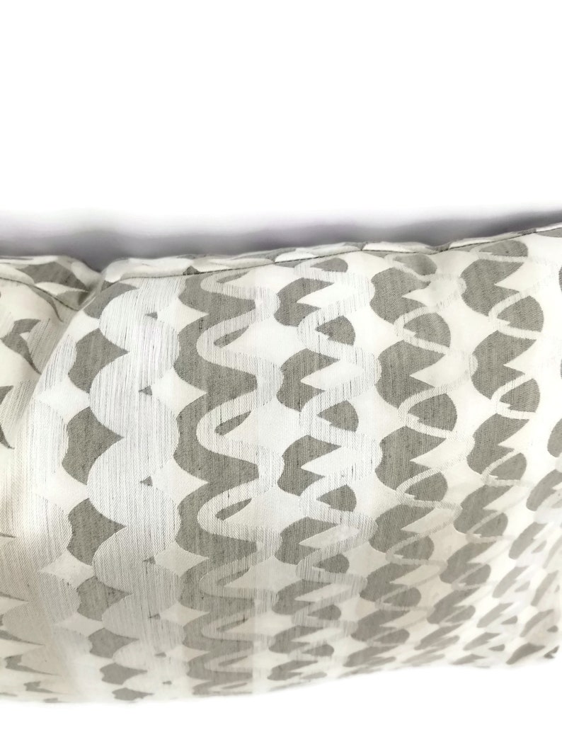 Puede incluir: Una almohada blanca con un patr&oacute;n geom&eacute;trico gris. El patr&oacute;n est&aacute; formado por formas curvas que se repiten.