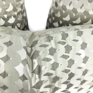 Puede incluir: Dos almohadas decorativas de color blanco roto con un patr&oacute;n tejido de c&iacute;rculos y espirales.