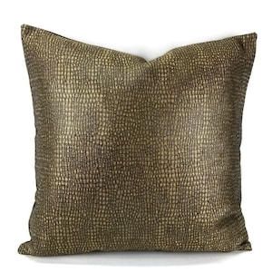 May include: Square decorative pillow with a textured, metallic gold surface. The pillow has a square shape and is likely used for home decor, adding a touch of luxury and style to any living space.