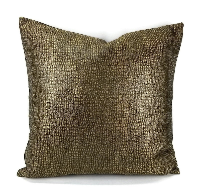 May include: Square decorative pillow with a textured, metallic gold surface. The pillow has a square shape and is likely used for home decor, adding a touch of luxury and style to any living space.