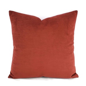 May include: A red velvet throw pillow with a subtle textured pattern. The pillow is square shaped and has a simple design.