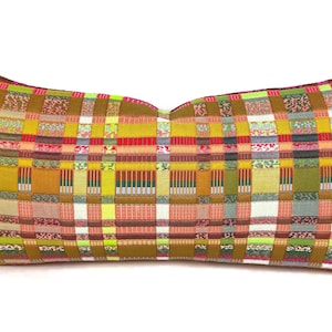 May include: A rectangular lumbar pillow featuring a vibrant woven plaid pattern. The textile displays a complex grid of mustard yellow, olive green, bright pink, white, and orange threads, creating a multi-colored checkered design throughout.