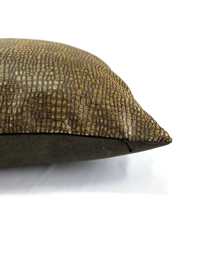 May include: Close-up of a decorative pillow with a textured, gold and brown pattern on the top surface. The bottom of the pillow is a solid dark green color. A black zipper is visible on the side.