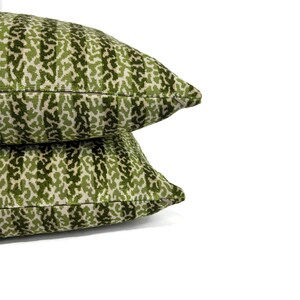May include: Two green and cream patterned throw pillows with a subtle striped design. The pillows are stacked on top of each other.