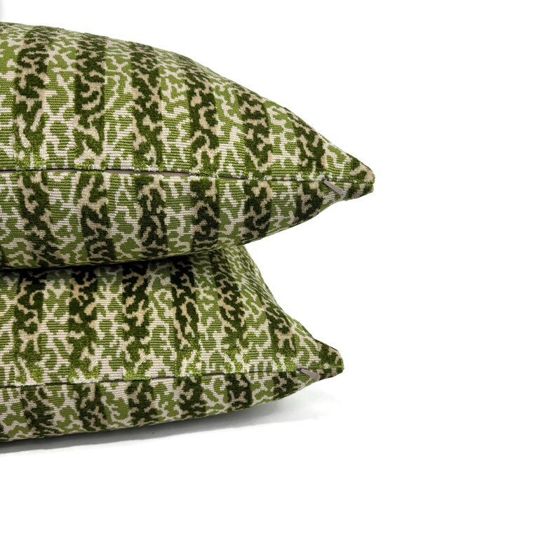 May include: Two green and cream patterned throw pillows with a subtle striped design. The pillows are stacked on top of each other.