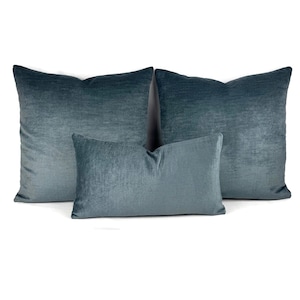 Puede incluir: Tres cojines decorativos cuadrados y rectangulares en un color azul cerceta oscuro s&oacute;lido. Los cojines presentan una textura de tela suave similar al terciopelo con un brillo sutil que refleja la luz en la superficie de cada coj&iacute;n de forma uniforme.
