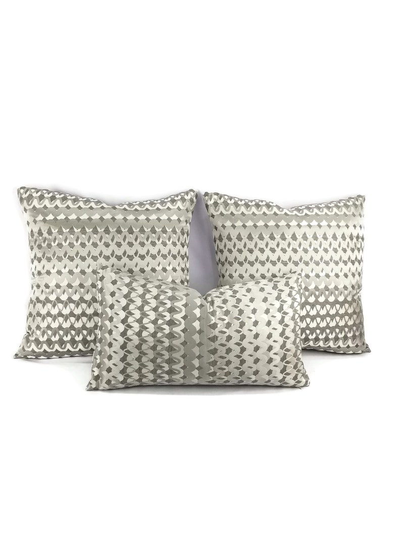 Puede incluir: Tres almohadas decorativas con un patr&oacute;n geom&eacute;trico en tonos grises y blancos.