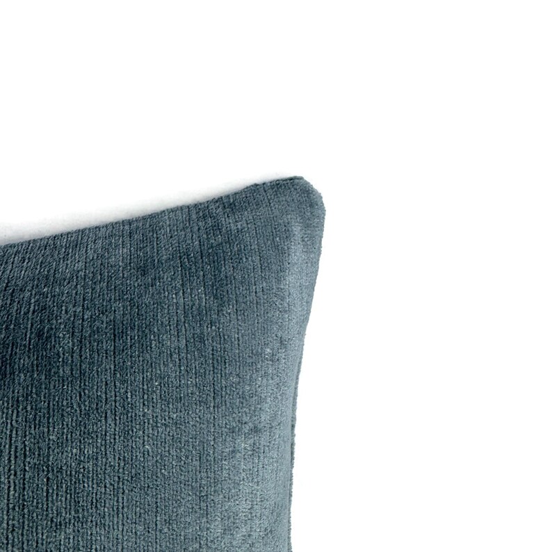 Puede incluir: Una esquina de un coj&iacute;n cuadrado de tela azul profundo texturizada con un patr&oacute;n de rayas verticales. El material tiene una apariencia suave y afelpada con variaciones sutiles en la profundidad del color en toda la superficie de la funda.