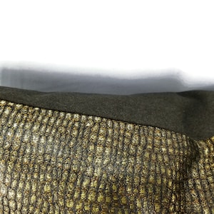 May include: Close-up of a section of fabric with a textured, gold and black pattern. The fabric has a woven appearance with a repeating geometric design. A dark green, solid-colored fabric is visible at the top of the image.