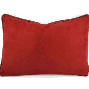 May include: A red rectangular pillow with a brown trim. The pillow is made of a soft, suede-like material.