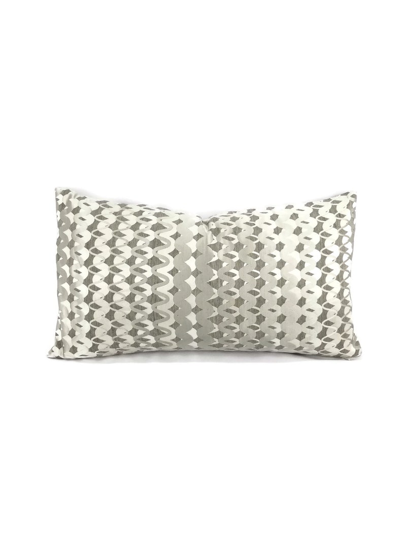 Puede incluir: Una almohada rectangular con fondo blanco y un patr&oacute;n geom&eacute;trico gris. El patr&oacute;n est&aacute; formado por formas repetidas que se asemejan a ondas o cadenas.