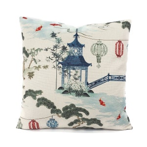 May include: A decorative throw pillow with a white background and a blue and white pagoda design. The pillow features red and green lanterns, a bridge, and gold fish.
