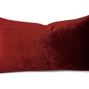 May include: A rectangular, burgundy-colored pillow with a textured, ribbed surface. The pillow is a solid color and appears to be made of a soft, plush material. The pillow is designed for decorative use.