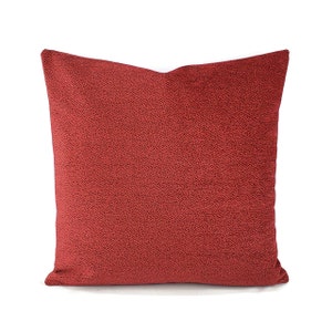 May include: A red throw pillow with a textured, speckled surface. The pillow is made of a soft, plush fabric.