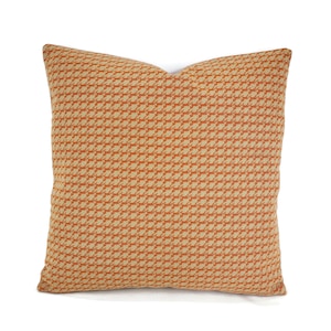 May include: A square throw pillow with a geometric pattern in shades of orange and beige.