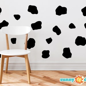 May include: A white wall with black cow spots decals, a white chair with wooden legs, and the text "sunny decals" in blue and orange at the bottom of the image.
