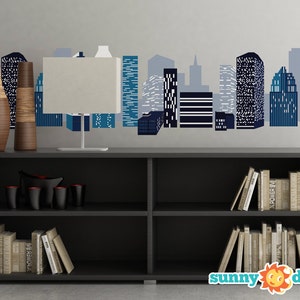 May include: A black bookshelf with two shelves, filled with books. The bookshelf is in front of a wall with a blue and white cityscape decal. Two brown vases are on top of the bookshelf.