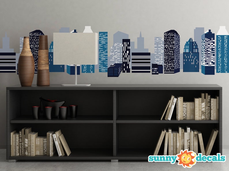 May include: A black bookshelf with two shelves, filled with books. The bookshelf is in front of a wall with a blue and white cityscape decal. Two brown vases are on top of the bookshelf.