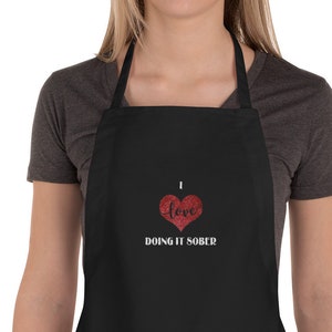 May include: Black apron with a red glitter heart and the text "I love doing it sober".