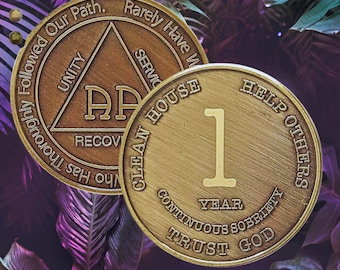 May include: A gold-colored coin with the text "Help Others" and "Clean House" on the top and bottom of the coin. The coin also has the text "Trust God" and "Continuous Sobriety" on the bottom. The coin has a large number "1" in the center and the text "Year" below it. The coin is surrounded by green and purple leaves.