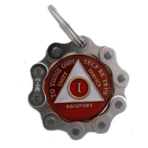May include: A silver keychain with a red and gold medallion featuring a triangle with the words "To thine own self be true", "Unity", "Service", and "Recovery". The medallion also has the Roman numeral "I" in the center.