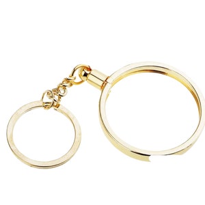 May include: A gold-colored key chain with a round coin holder attached to a key ring. The coin holder has a small opening on the side.