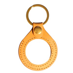 May include: A tan leather keychain with a brass key ring and a stitched circle in the center.