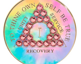 May include: A round, colorful, tie-dye patterned coin with a gold rim. The coin features a triangle with the words "To Thine Own Self Be True" and "Unity, Service, Recovery" around the triangle. The triangle is filled with pink rhinestones and the number "I" is in the center.