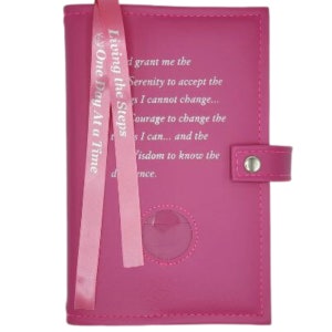 May include: A pink leather journal with a pink ribbon bookmark. The ribbon has the text "Living the Steps One Day At a Time" printed on it. The journal has a clear plastic window on the front cover and a quote about serenity, courage, and wisdom printed on the front cover.