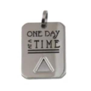 May include: A silver-colored rectangular pendant with the words "ONE DAY AT A TIME" engraved on the front. Below the text is a triangle symbol. The pendant has a loop at the top for a chain.