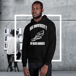 Könnte beinhalten: Schwarzer Kapuzenpullover mit weißem Text und Grafik. Der Text lautet "DIS UNIVERSITY" über einer Grafik eines geflügelten Laufschuhs mit "LOS ANGELES" und "OF HARD KNOCKS" darunter. Der Kapuzenpullover wird von einer Person getragen.