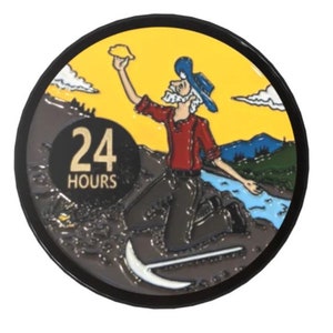 Puede incluir: Un pin redondo con borde negro y fondo amarillo. Un prospector de dibujos animados con camisa roja y sombrero azul sostiene una pepita de oro. El texto "24 HORAS" está en un círculo negro en la esquina inferior izquierda.