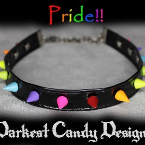 Puede incluir: Un collar de cuero negro con pinchos de colores arcoíris. El collar tiene el texto "Pride!" arriba y "Darkest Candy Designs" abajo.