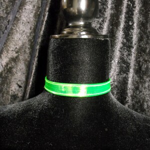 May include: A neon green choker necklace with a white border is displayed on a black mannequin. The text "Darkest Candy Designs" is at the bottom of the image. The choker is a vibrant accessory.