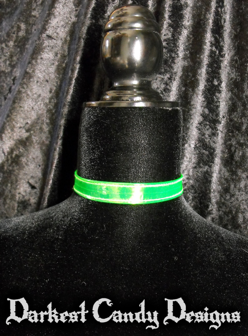 May include: A neon green choker necklace with a white border is displayed on a black mannequin. The text "Darkest Candy Designs" is at the bottom of the image. The choker is a vibrant accessory.