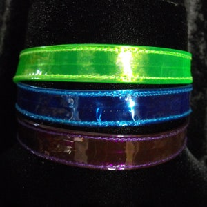 May include: Three colorful chokers in green, blue, and purple. Each choker is made of a shiny, transparent material with a stitched edge. The text "Darkest Candy Designs" is at the bottom.