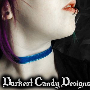 May include: A close-up of a blue velvet choker necklace. The choker is worn around the neck. The text "Darkest Candy Designs" is displayed in a gothic font at the bottom of the image.